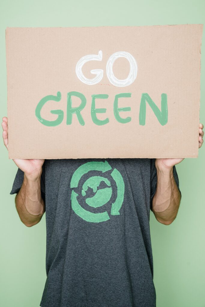 Uomo che indossa una maglia con il pianeta terra, in verde, circondato dalle frecce simbolo del riciclo e che sorregge un cartello con lo slogan "Go green"