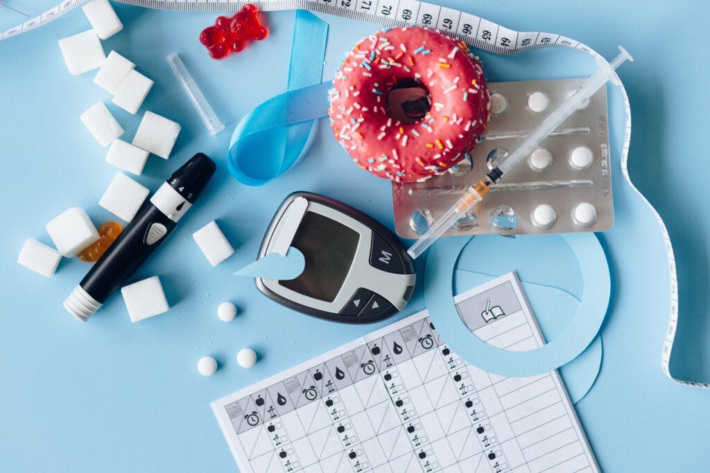 Diversi oggetti associati al diabete e all'insulina:un lettore della glicemia, una siringa di insulina, compresse, un metro, una ciambella glassata, zollette di zucchero e un calendario della glicemia