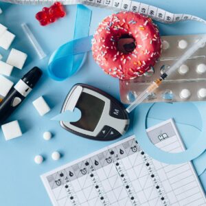 Diversi oggetti associati al diabete e all'insulina:un lettore della glicemia, una siringa di insulina, compresse, un metro, una ciambella glassata, zollette di zucchero e un calendario della glicemia