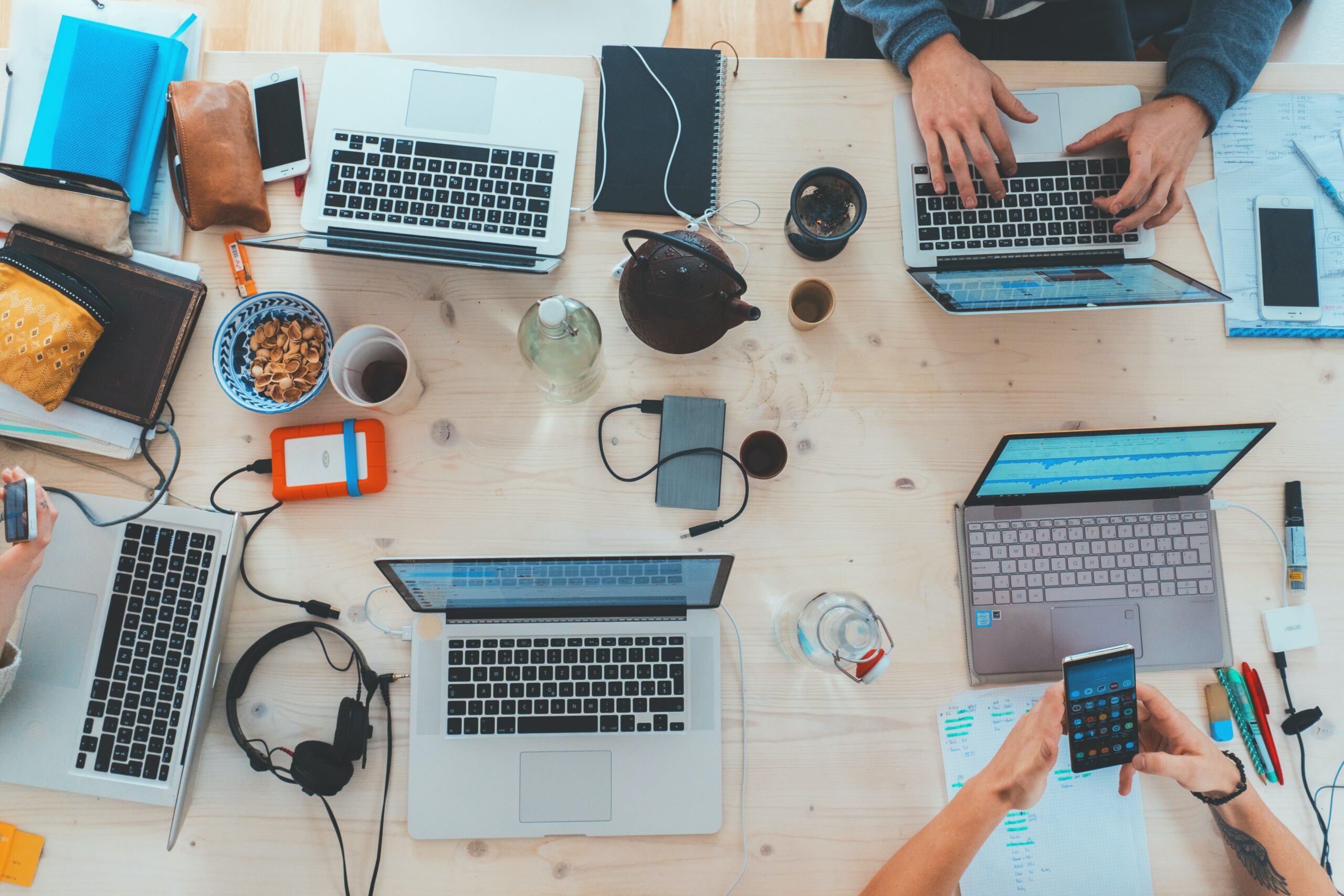 Scrivania disordinata vista dall'alto con diversi laptop, cuffie e tazze di caffè