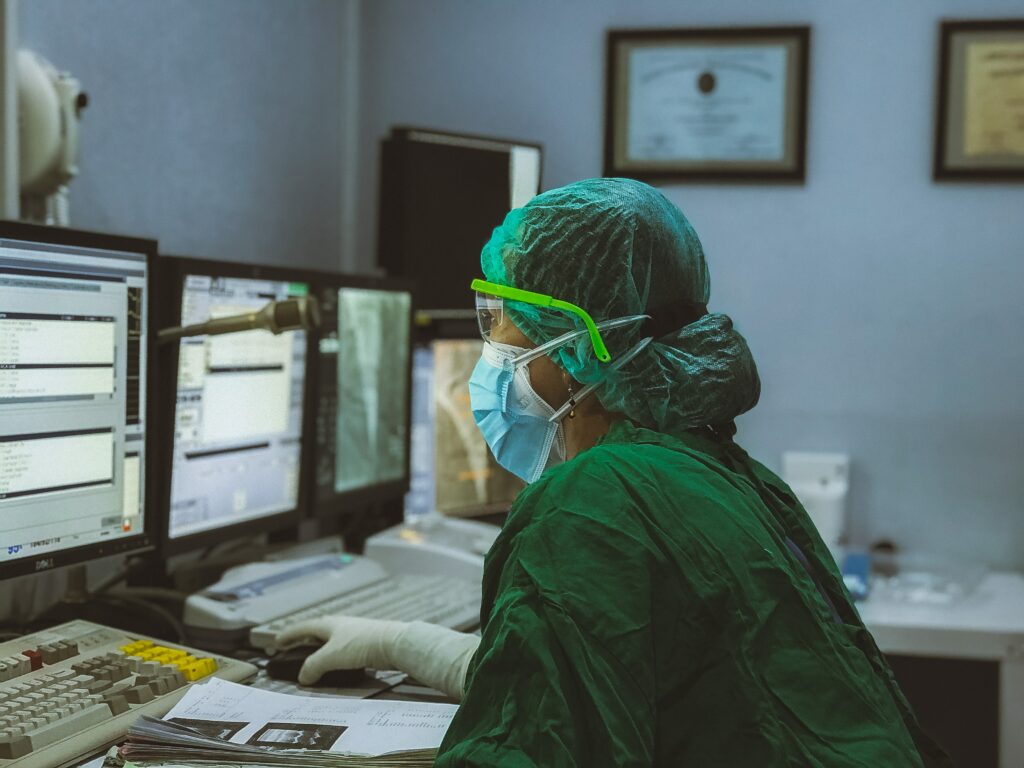 Operatore sanitario in divisa e mascherina che lavora al pc su un software medico