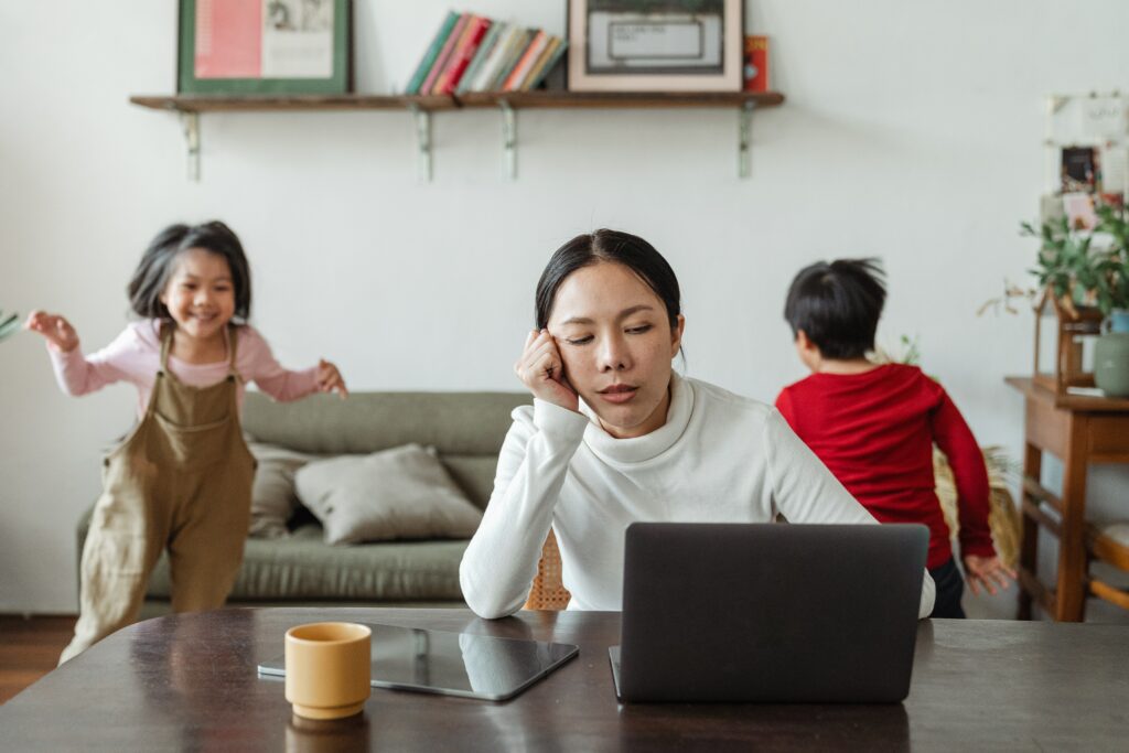 Donna assonnata che lavora al pc con i figli che giocano sullo sfondo